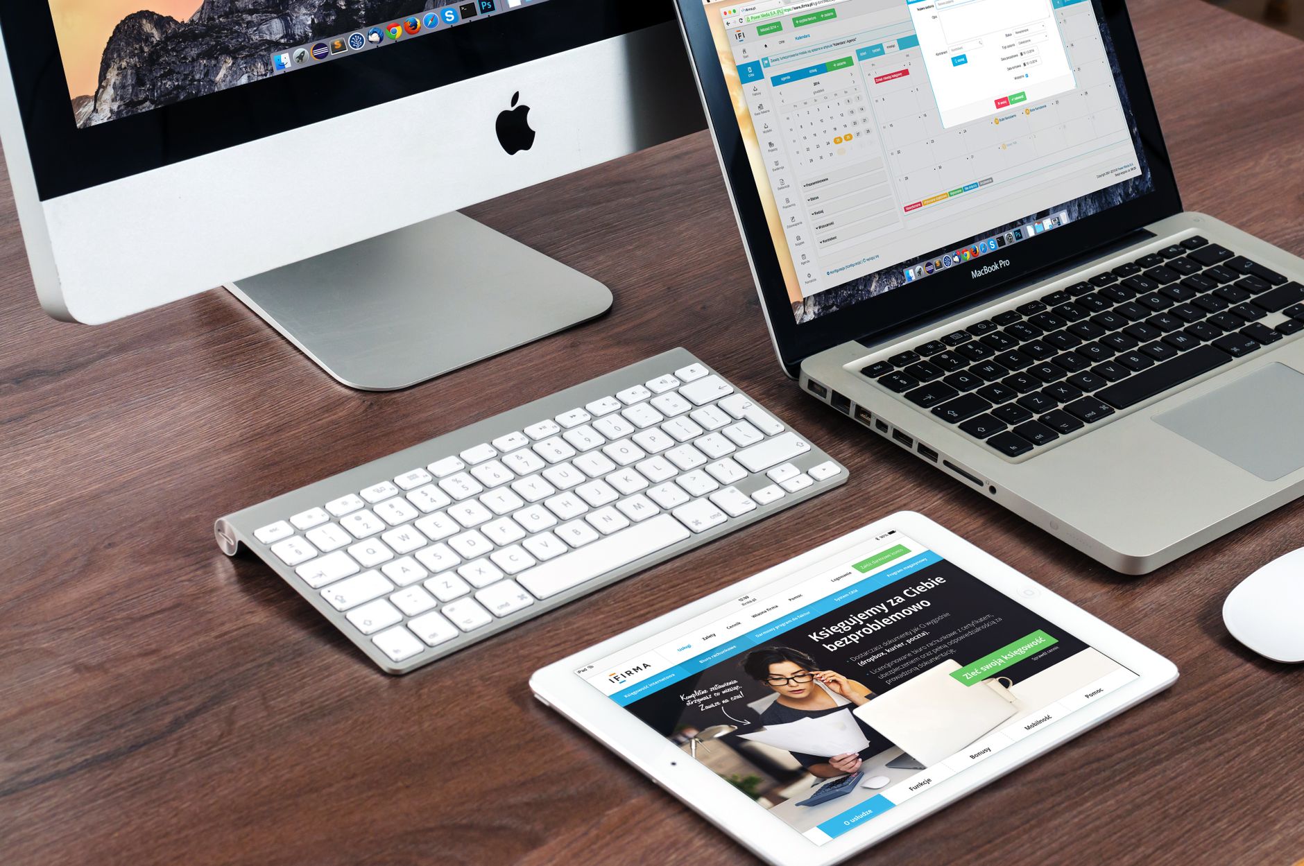 Imac, MacBook e tablet sobre uma mesa exibindo diferentes páginas de um site