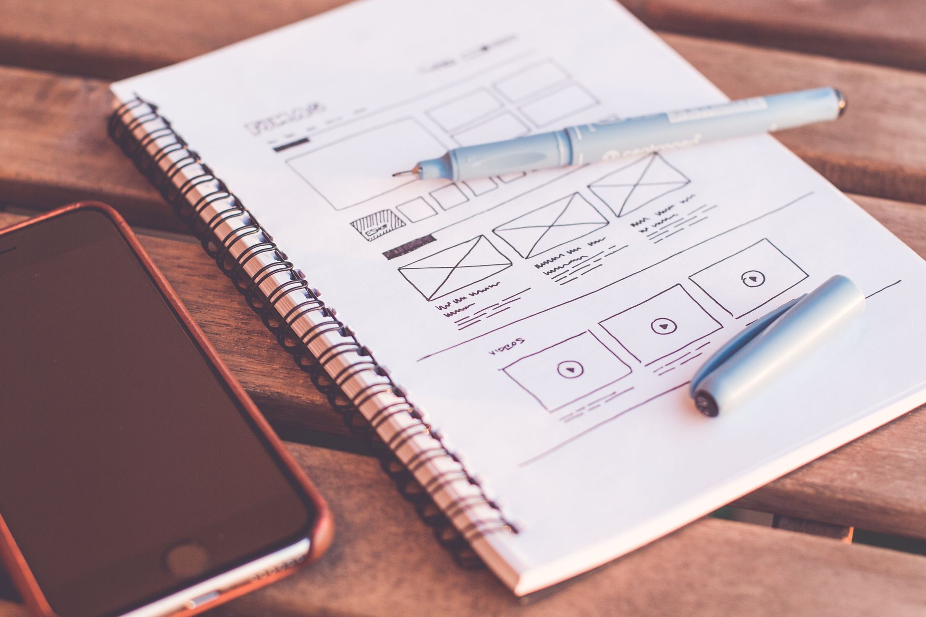 Caderno com wireframe de site desenhado à mão ao lado de um smartphone sobre a mesa