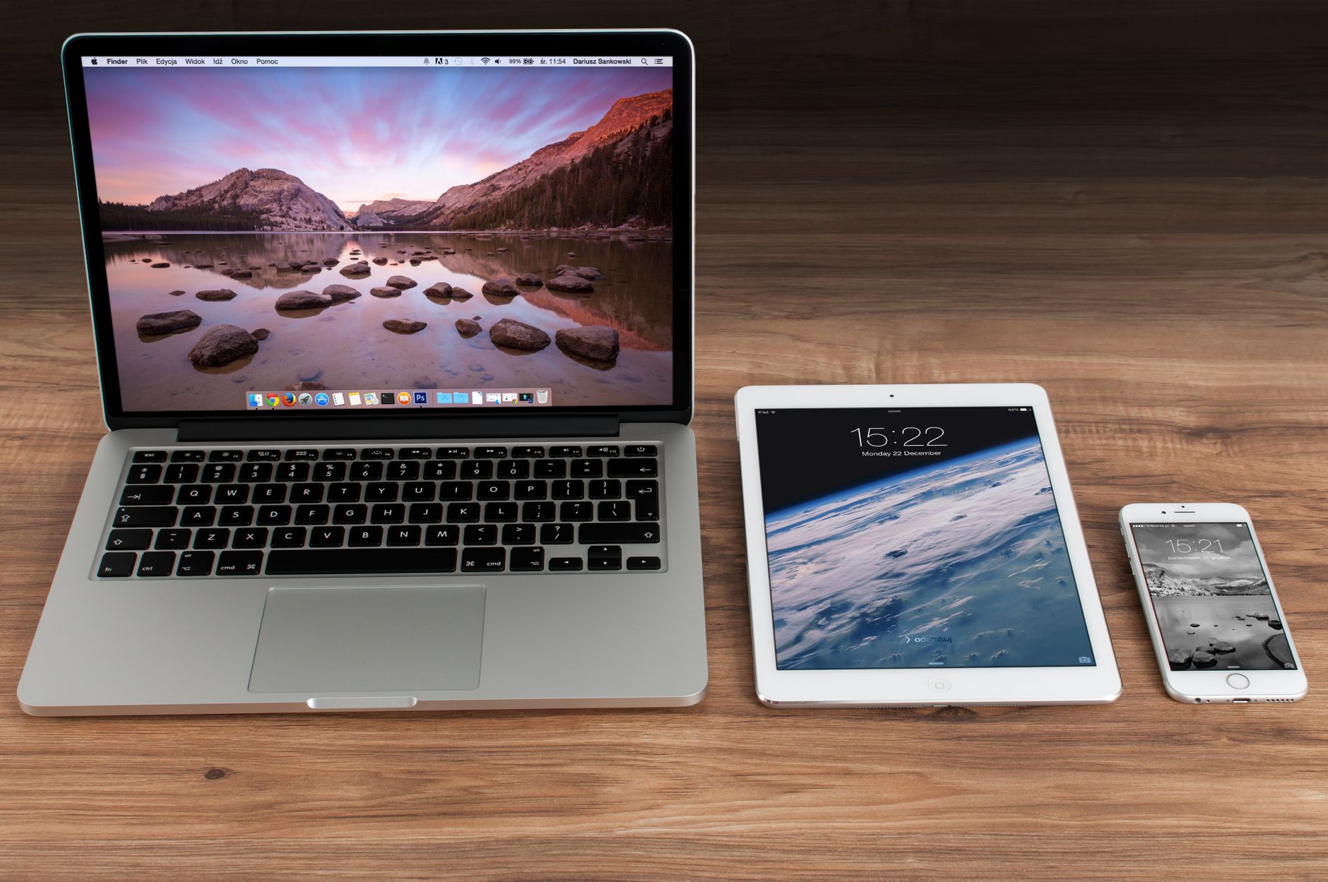 Laptop, tablet e smartphone lado a lado sobre uma mesa de madeira, cada um exibindo uma tela diferente