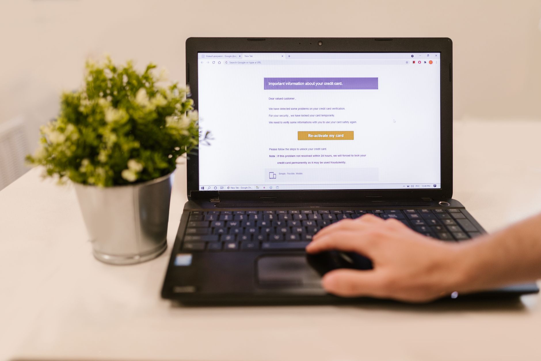 Pessoa usando o mouse em um laptop que exibe uma mensagem na tela, com um vaso de flores ao lado sobre a mesa