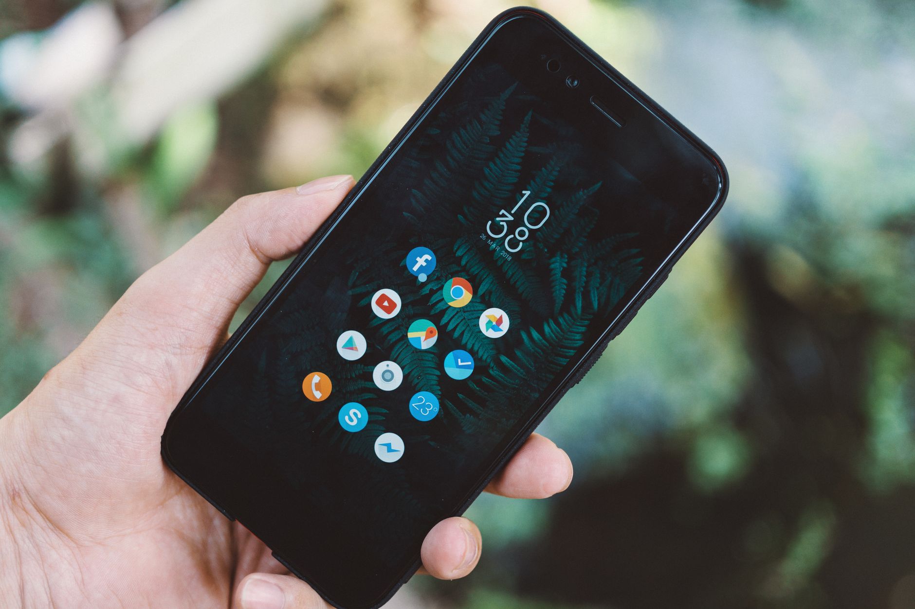 Pessoa segurando um smartphone ao ar livre, com ícones de aplicativos como Facebook, Chrome e Maps na tela