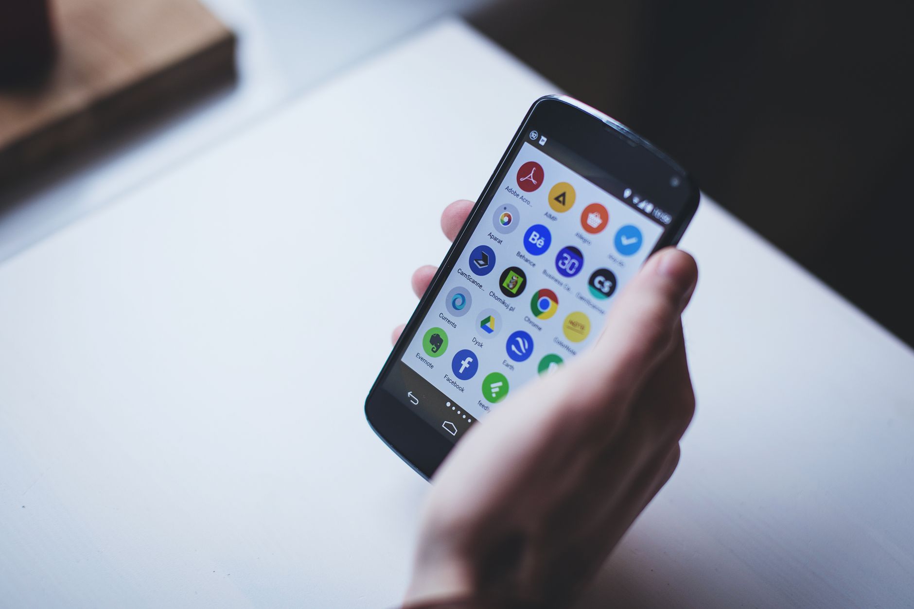 Mão segurando um smartphone exibindo diversos ícones de aplicativos de produtividade, como Evernote, Dropbox e Chrome